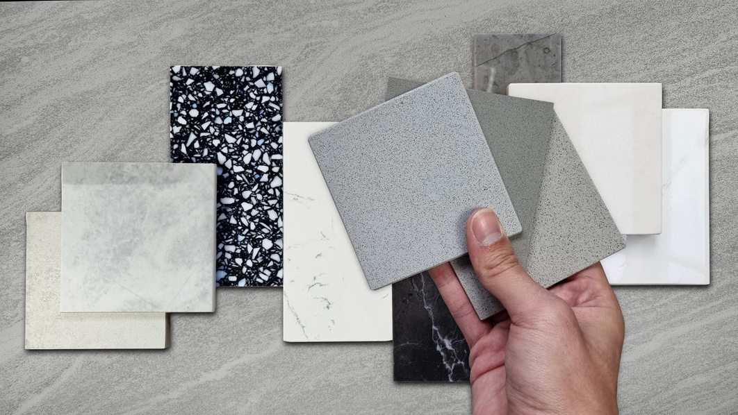 interior designer compaing set of grainy quartz samples with black marble, grey artificial stone, terrazzo tiles samples. countertop or tabletop furnishing material samples on travertine background.